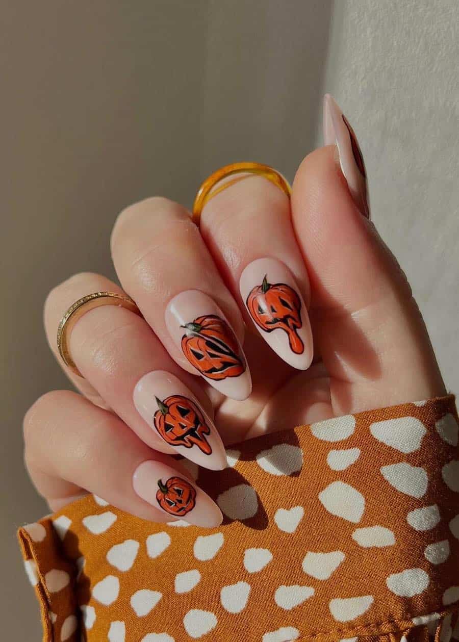 a hand with long almond nails painted a white nude with drippy pumpkin nail art