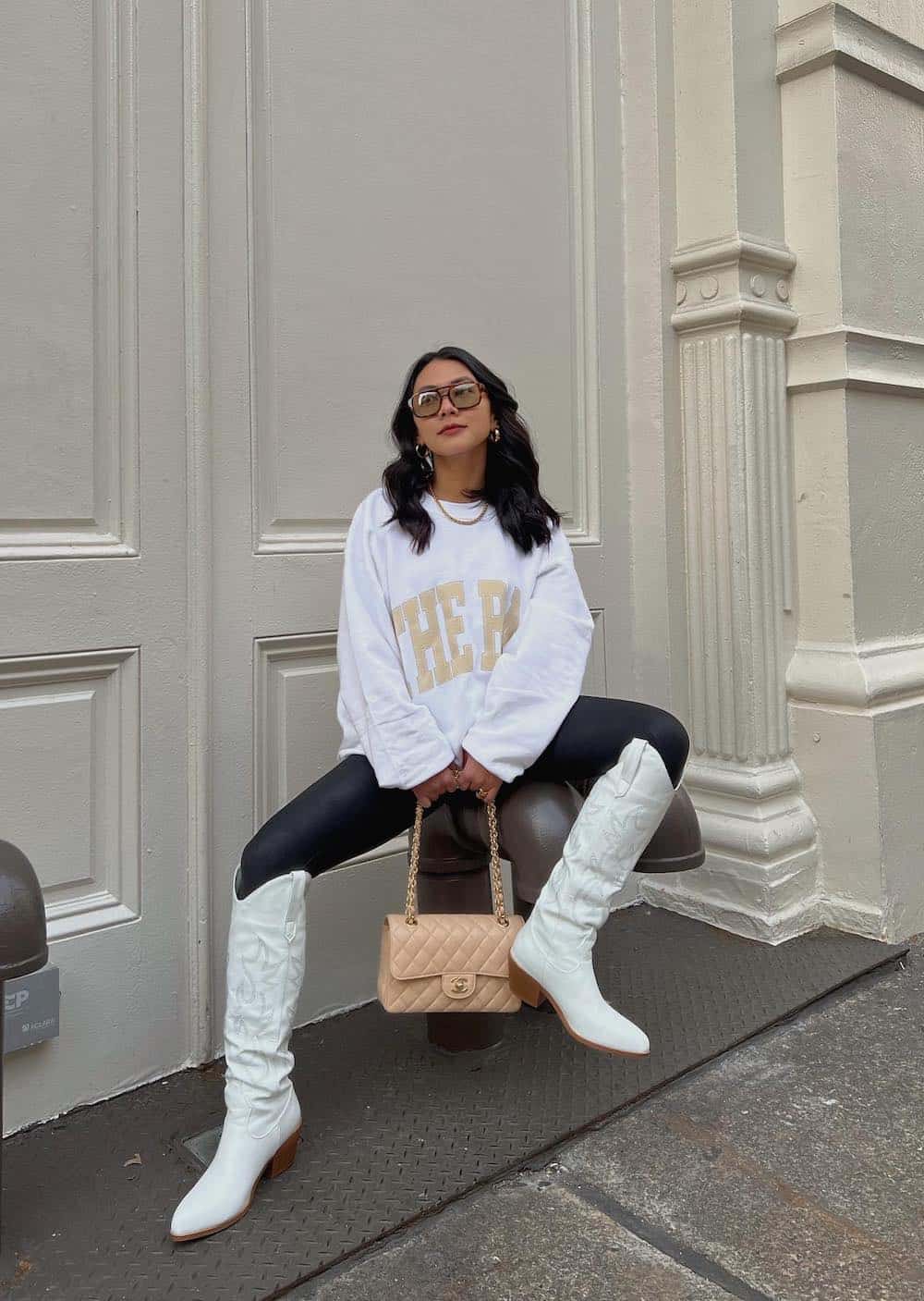 woman wearing an oversized white sweatshirt with leather leggings and white cowboy boots