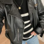 close up of a woman wearing a black leather jacket over a black striped sweater