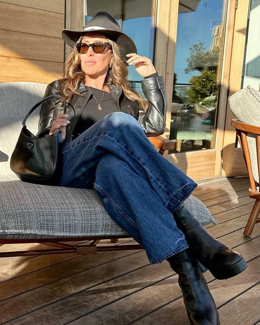woman over 50 wearing a Nashville outfit with a black leather jacket, jeans, fedora, and black boots
