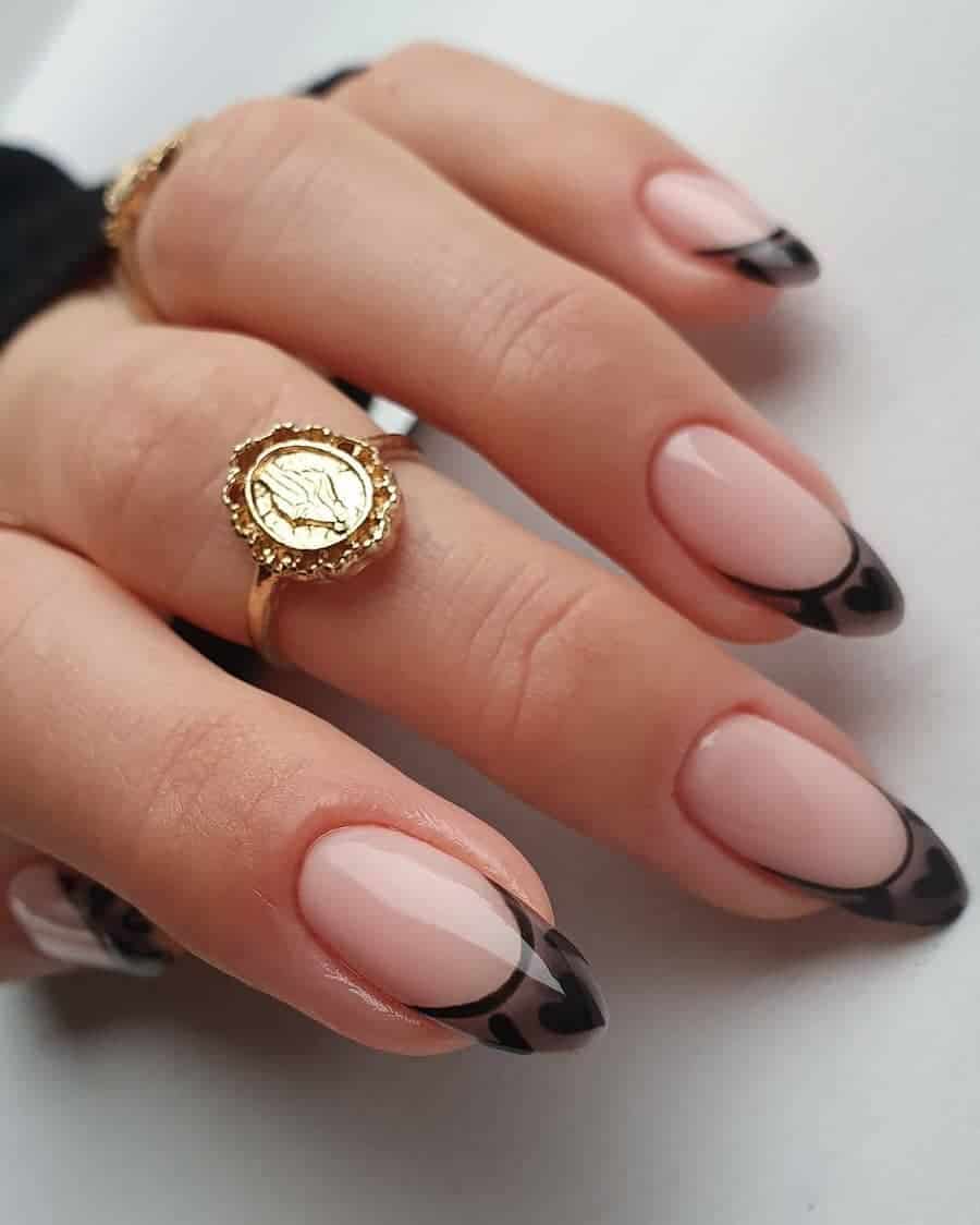 Rounded nails with a nude background and black transparent french tips with opaque black heart detail.
