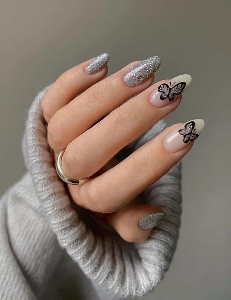 Long silver glitter nails with black and silver glitter butterfly details.