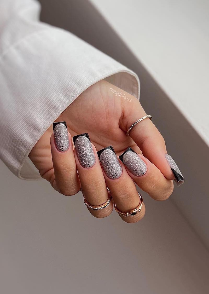 Square silver glitter nails with black french tips and black dot detailing.