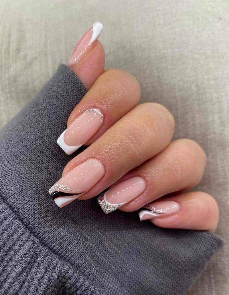 Square nude nails with white french tips and black and silver glitter wave detailing.