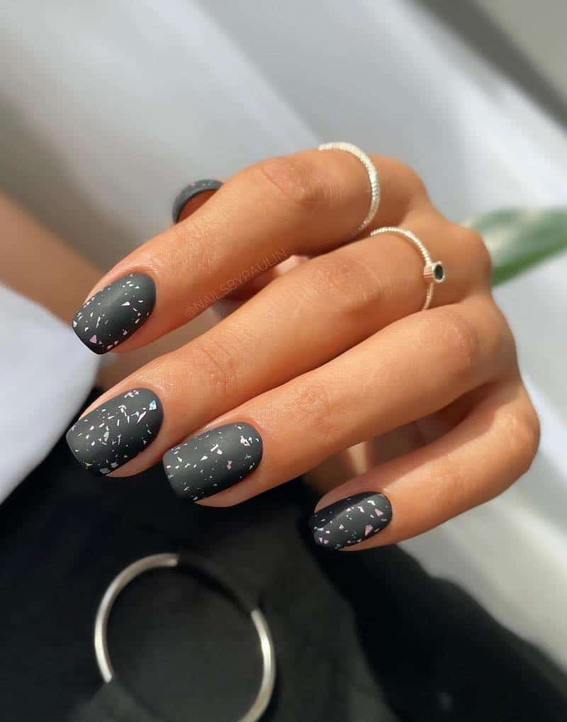 Short, matte black nails with white paint fleck details.