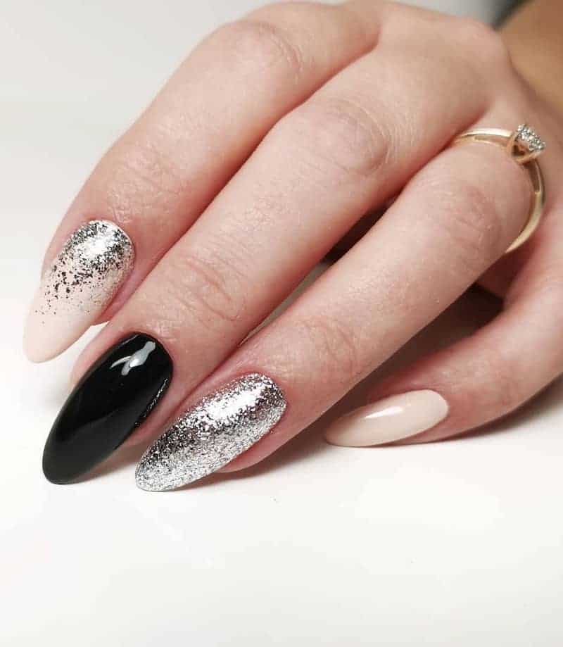 Mismatched manicure with a black glossy nail, nude nail, silver foil glitter nail and nude nail with silver glitter ombre.