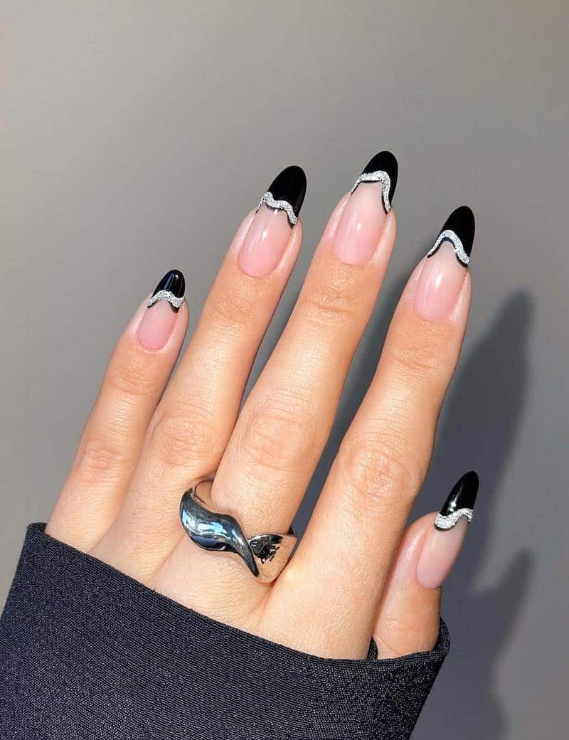 Black french tip manicure with silver glitter wave detailing.
