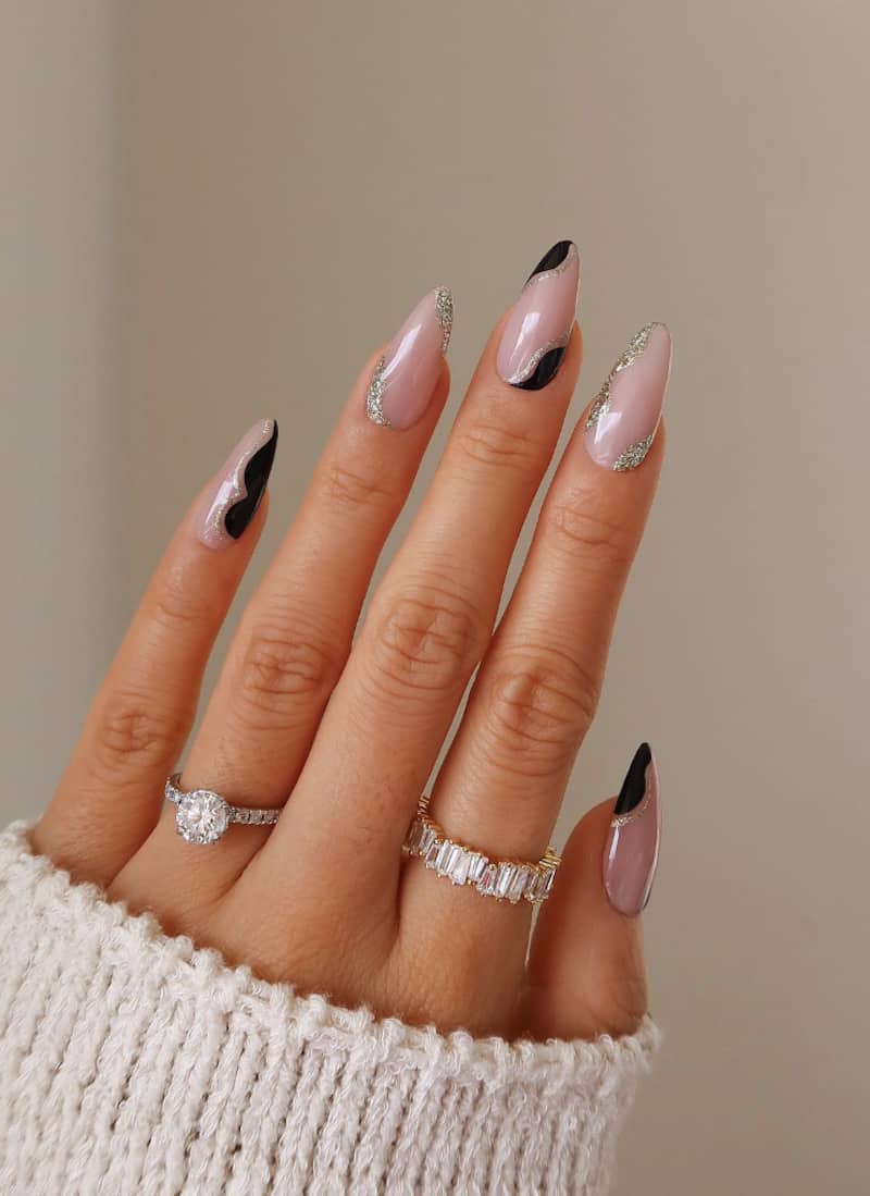 Nude nails with black and silver glitter wave detailing.