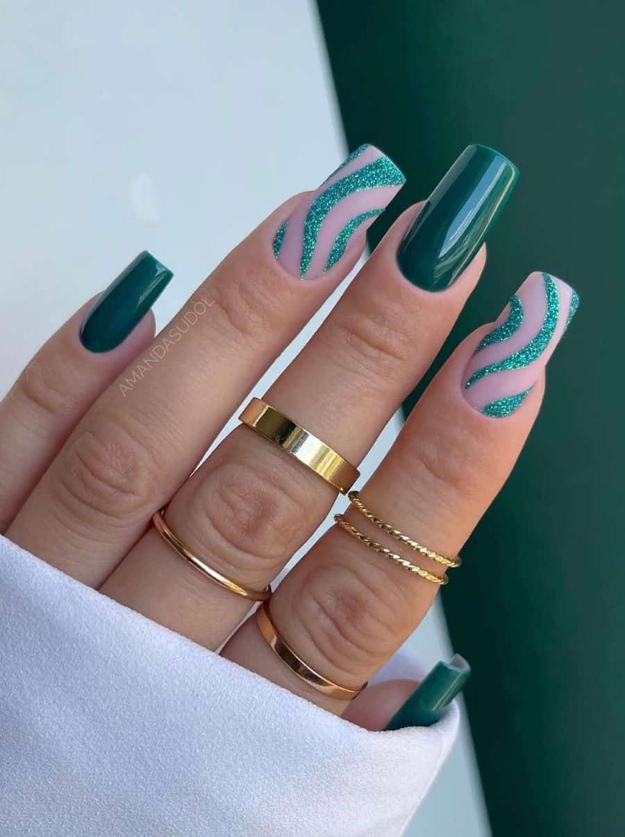 A hand with medium-long square nails painted with glossy emerald green polish with two matte nude accent nails with glittery green waves