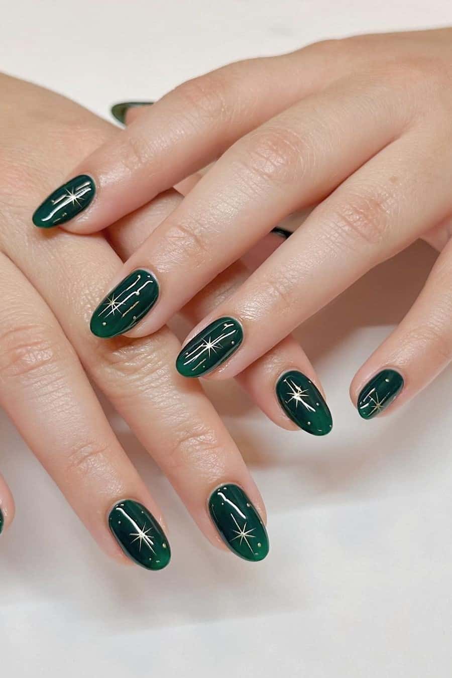 A hand with short round nails painted a glossy emerald green with gold sparkles and dot details