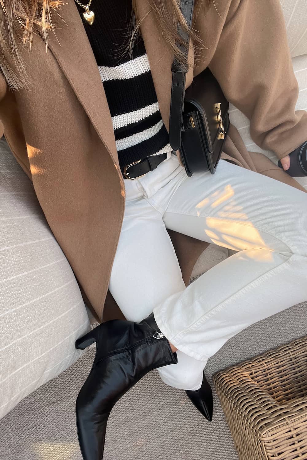 woman wearing a camel coat over a striped knit sweater with off-white jeans and black pointed boots for a fall capsule wardrobe outfit