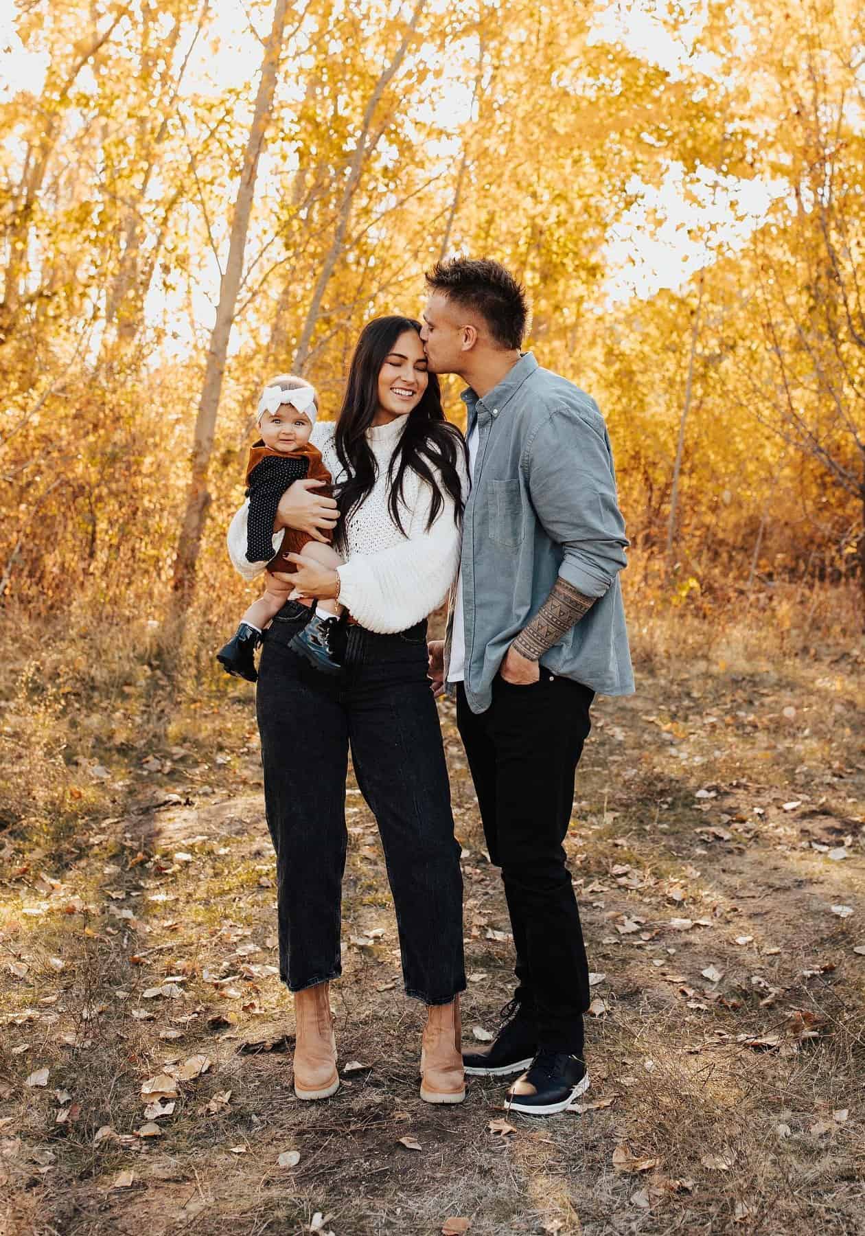 A family photo in fall with a mom, dad, and baby girl dress in neutral colors