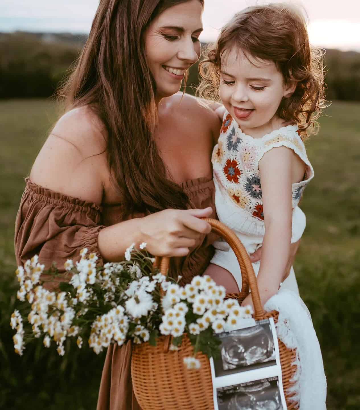 A mother and daughter during a spring family photoshoot with a basket of flowers with ultrasound photos