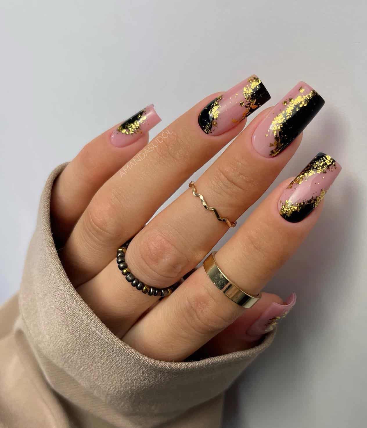 Long square nails with nude and black polish and gold glitter details