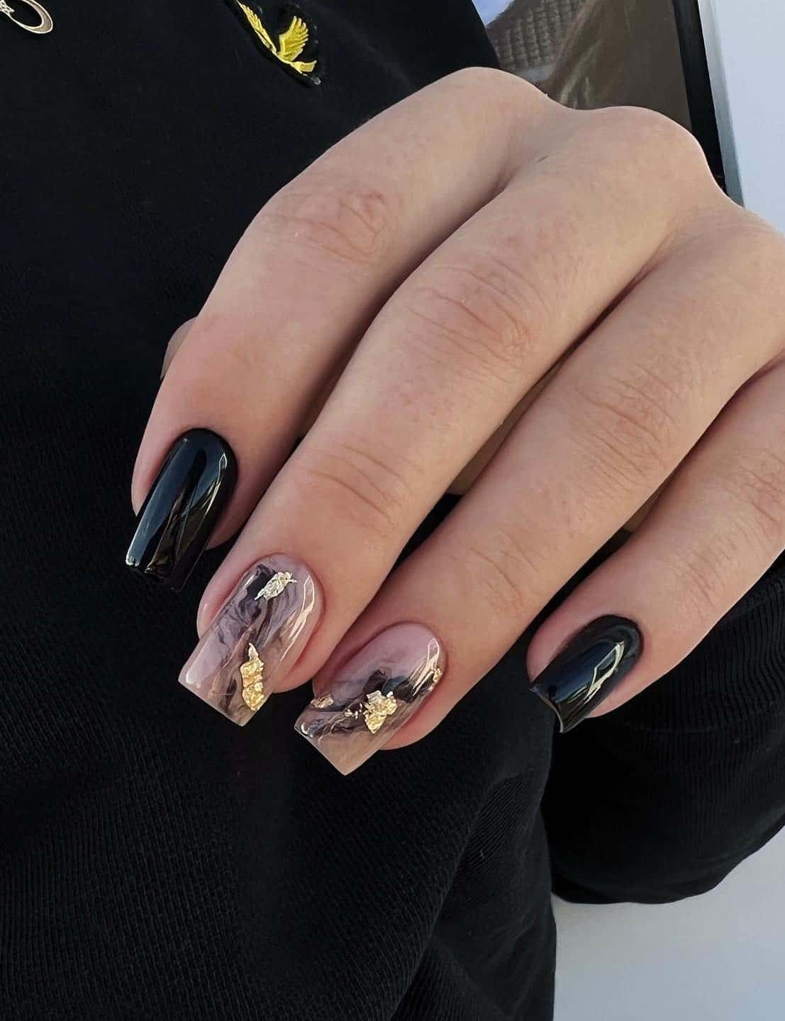 Medium square nails with glossy black polish and nude and black marbled accent nails with gold flakes