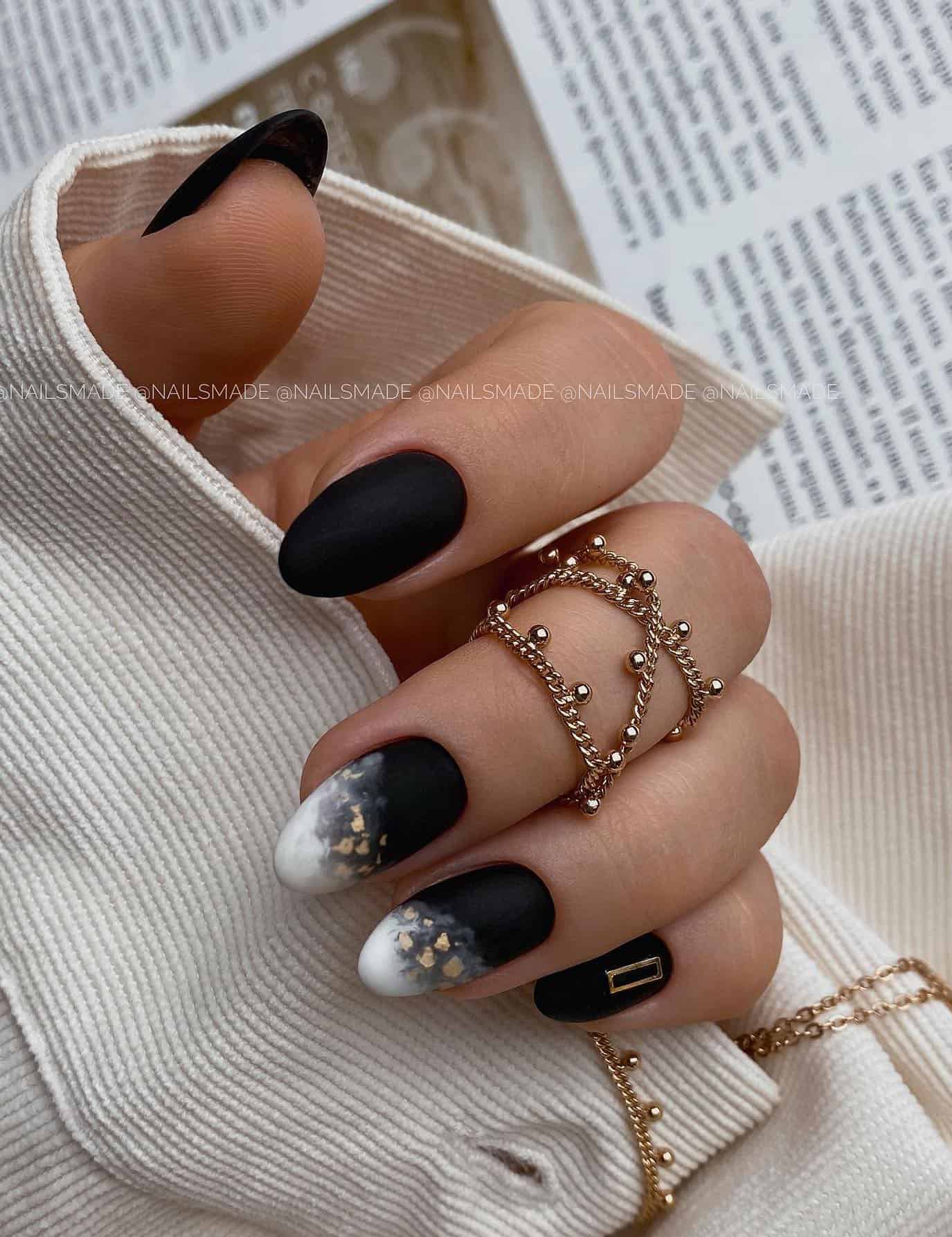 Short matte black almond nails with white and black ombre accent nails and gold flakes