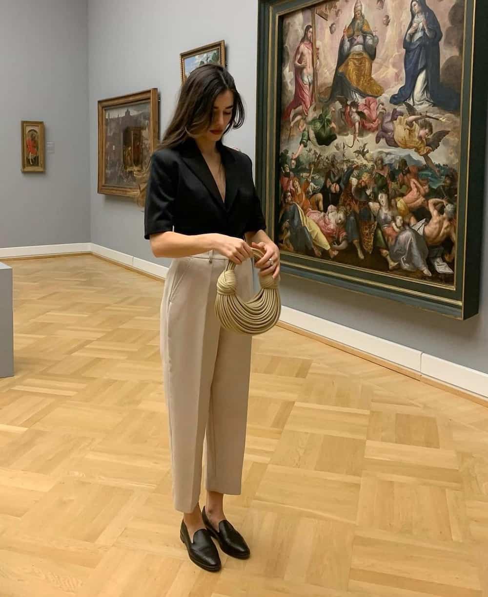 Woman wearing tan trousers and a black blouse in a museum.