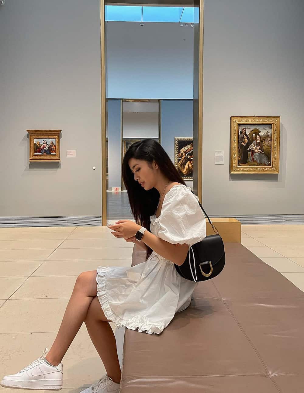 Woman wearing a white babydoll dress and white sneakers in a museum.