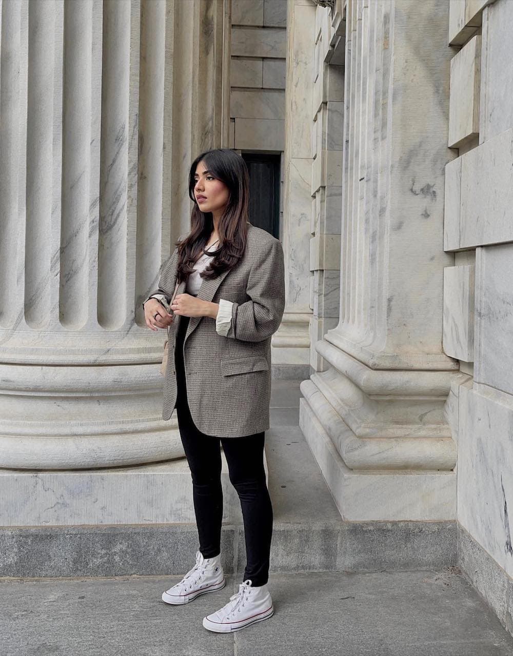 Woman wearing black leggings and an oversized blazer with Chuck Taylors outside of a museum.