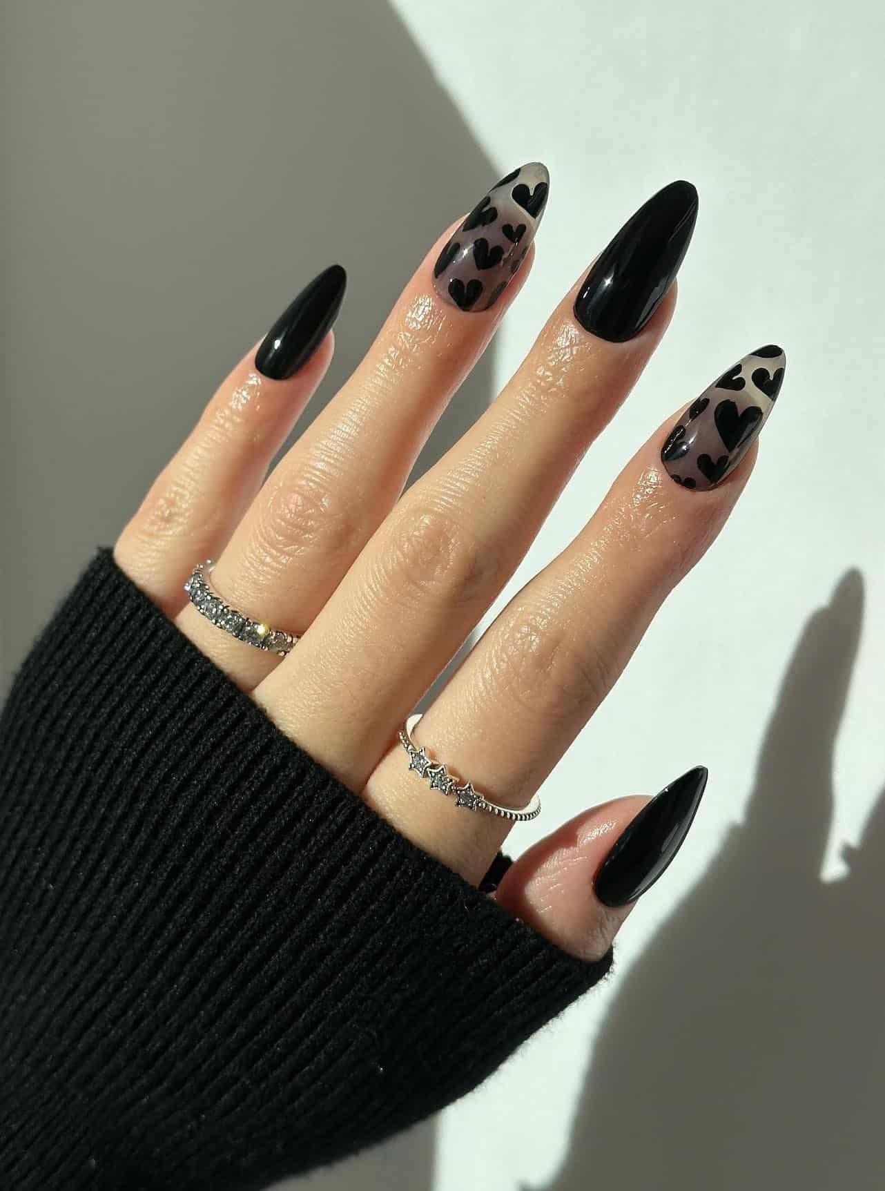Long almond nails with glossy black polish and sheer black accent nails with heart art
