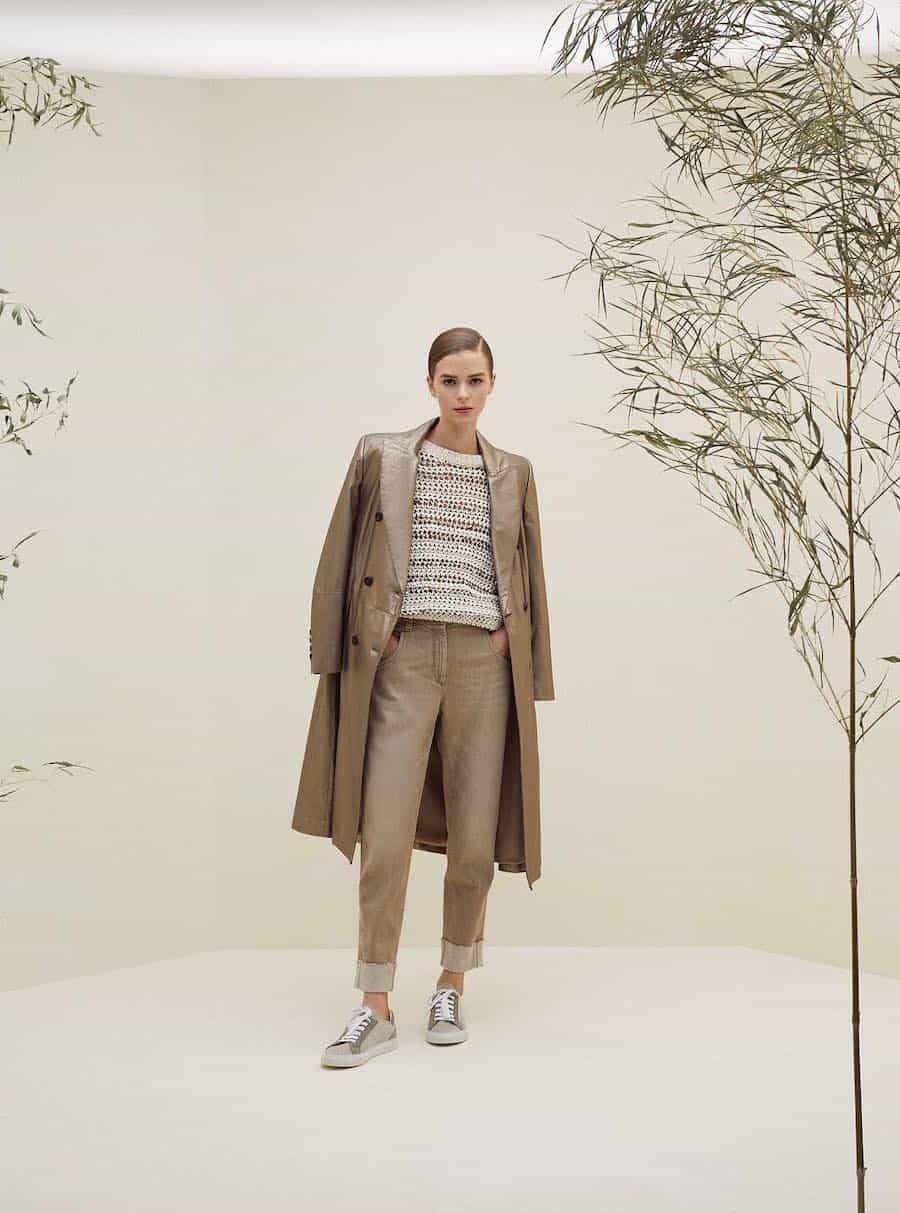 A woman wearing beige jeans, a white and beige striped sweater, a beige leather coat, and brown and beige sneakers