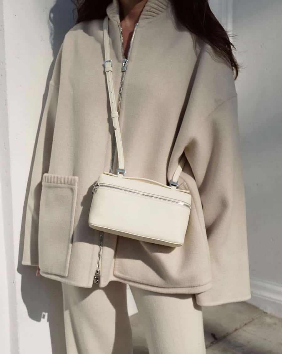 A woman wearing a matching beige set with a white leather crossbody purse