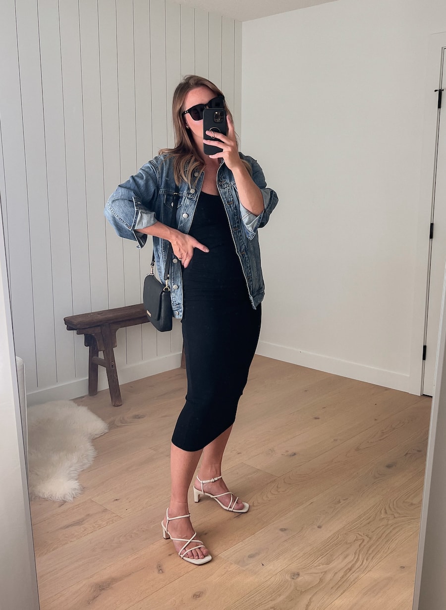 woman wearing a black midi dress with white heeled sandals and a denim jacket 