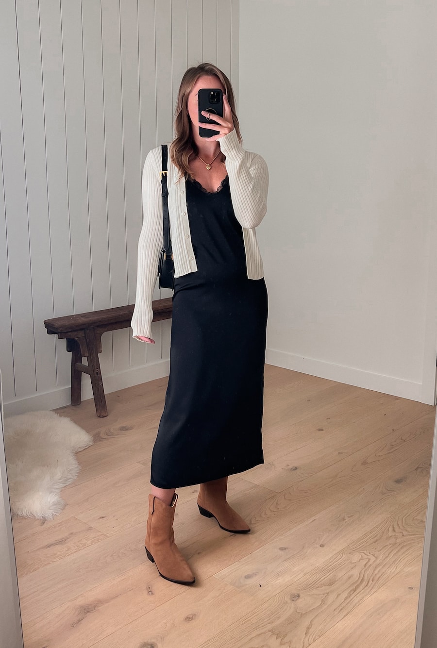 woman wearing a long black slip dress with brown western style boots and a knit ivory cardigan