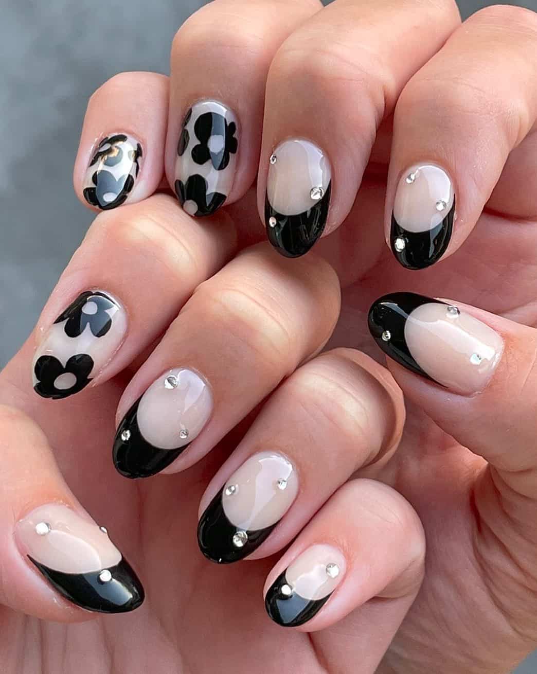 Short nude nails with black French tips, black floral art nails, and gem accents