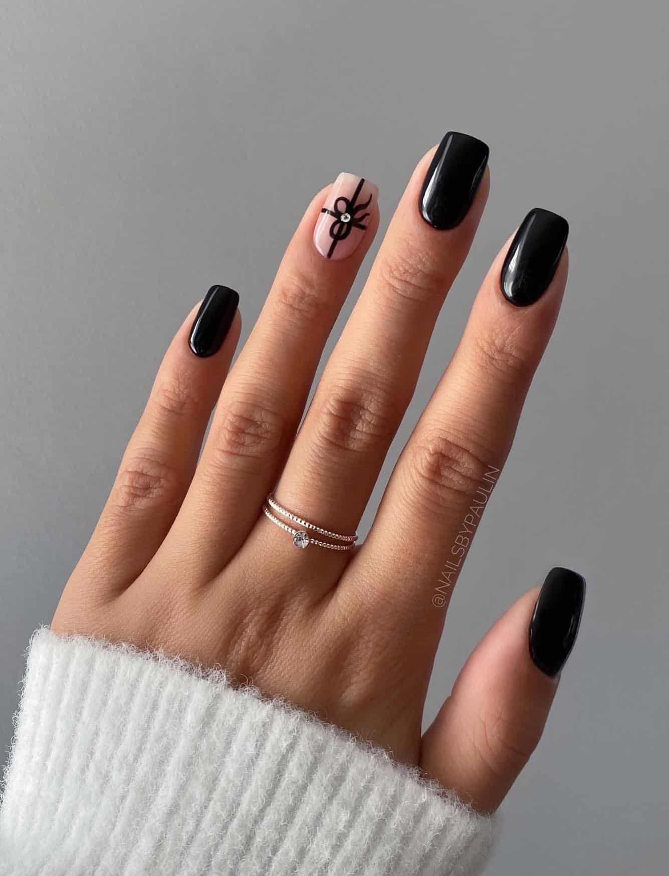 Short glossy black square nails with nude accent nail painted like a present with black ribbon and a gem detail