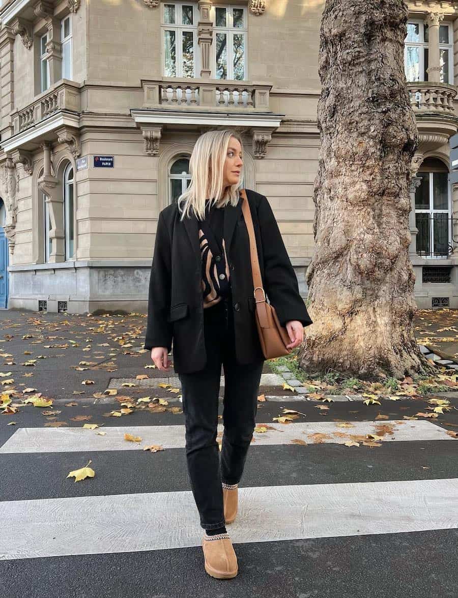 A woman wearing brown slippers with black jeans, a patterned cardigan, and a black blazer