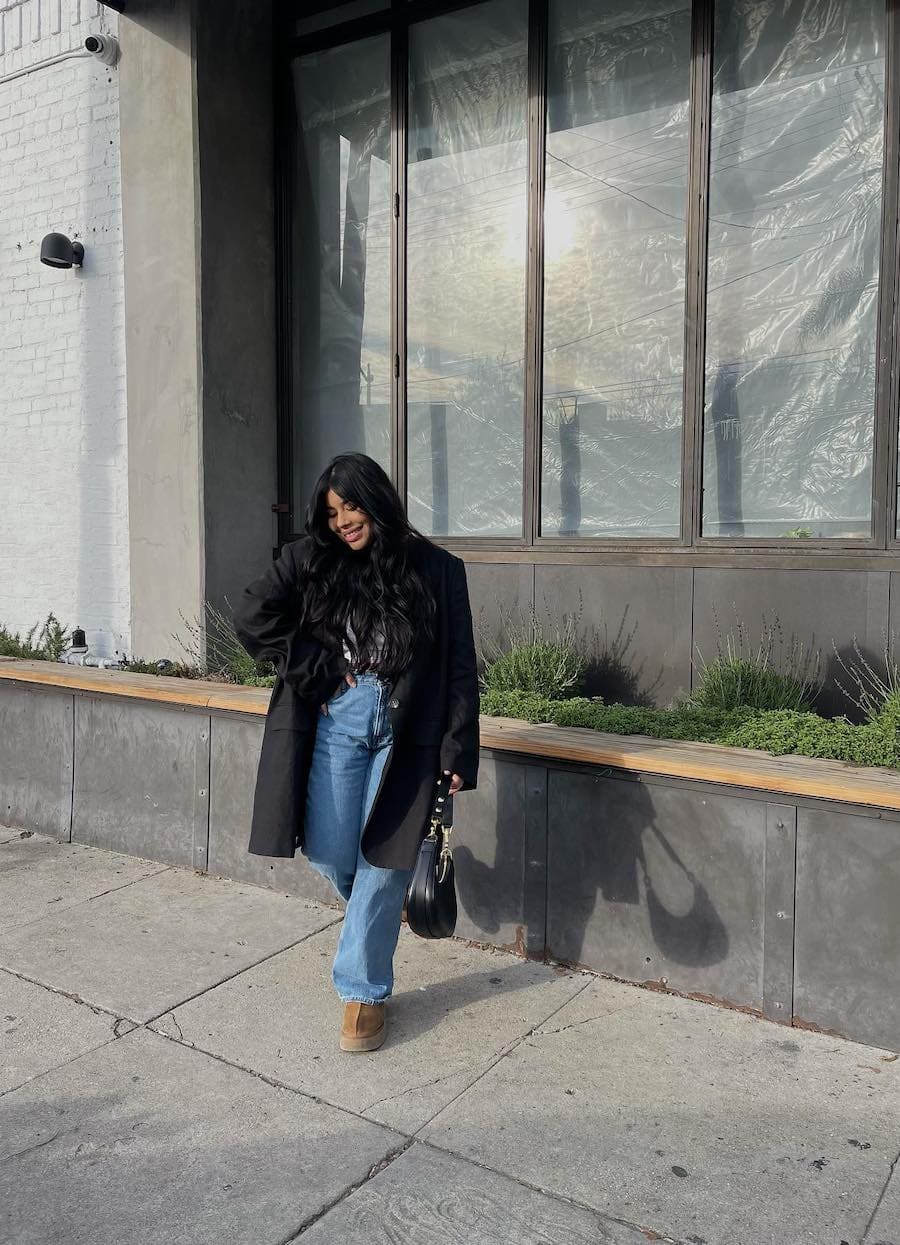 A woman wearing blue jeans with brown slippers and an oversized black coat