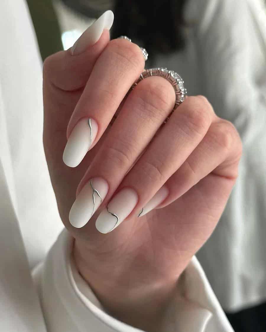 Long almond nails with a white and nude matte ombre and silver accents