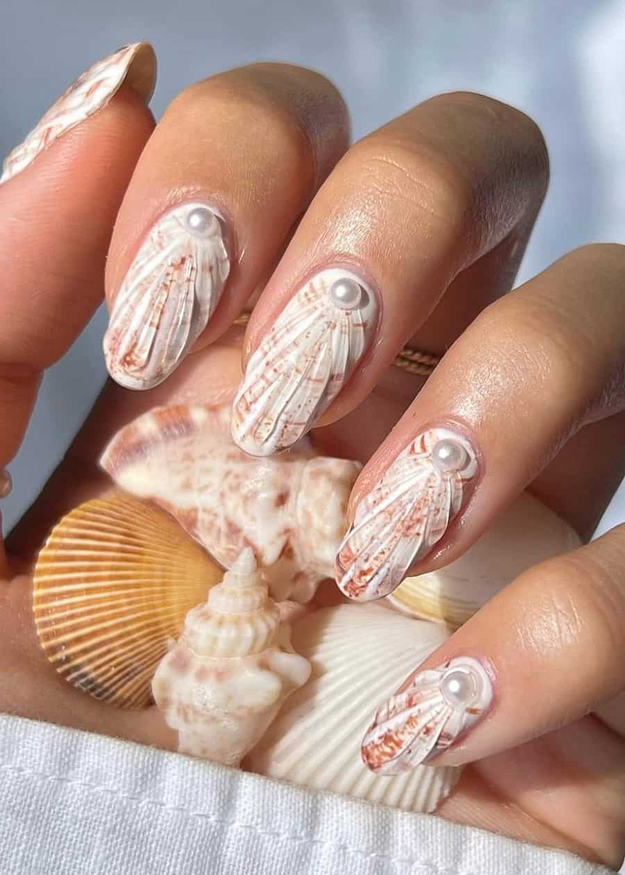 Short almond nails painted like white seashells with specks of brown and pearl accents