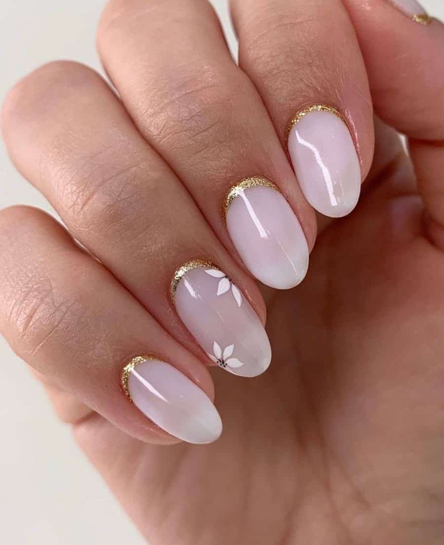 Short milky white almond nails with gold glitter reverse French tips and white floral art accents