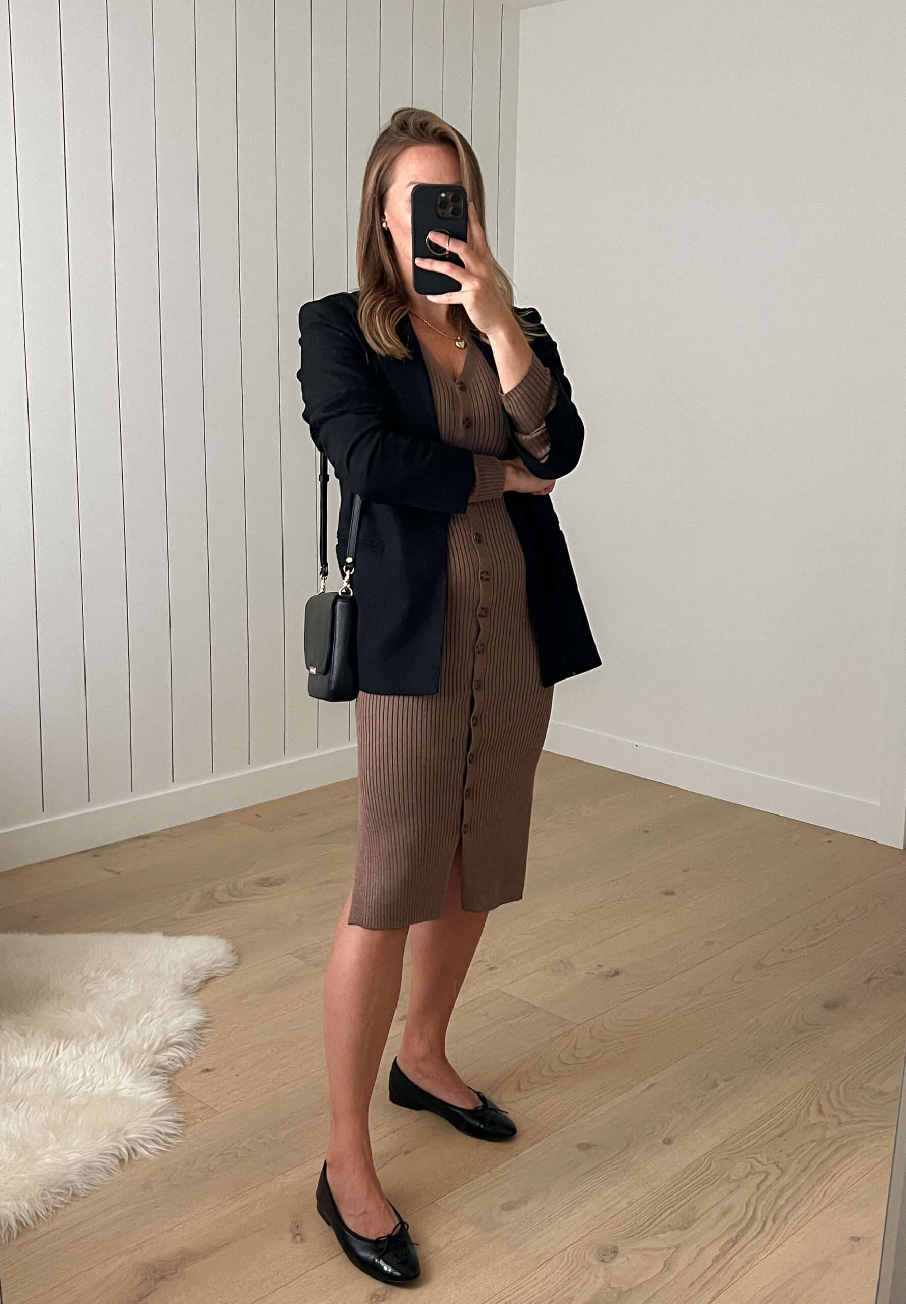 Woman wearing a brown knee length midi dress with black balet flats and a black blazer