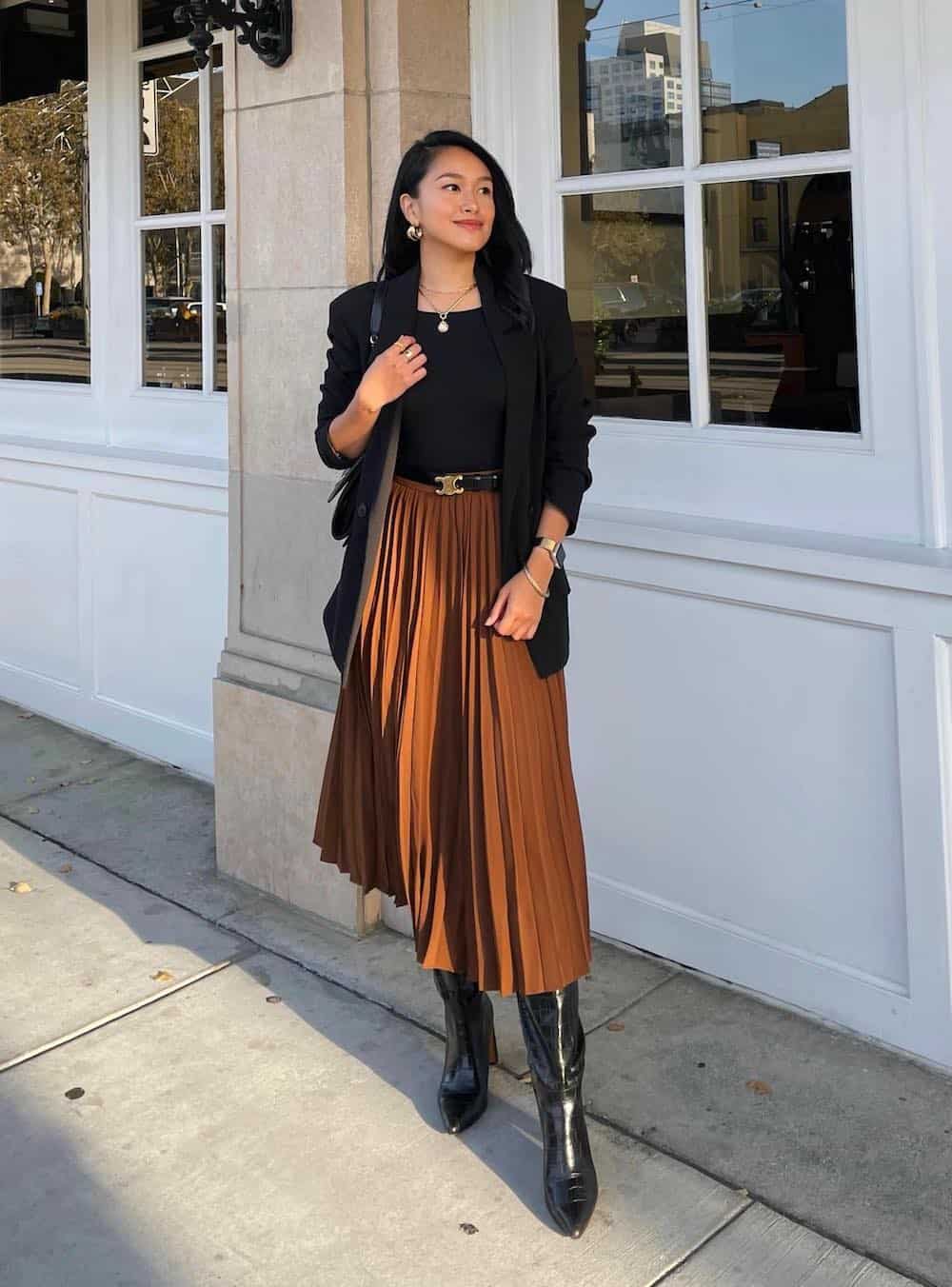 Woman wearing black boots and a brown midi skirt with a black blazer.