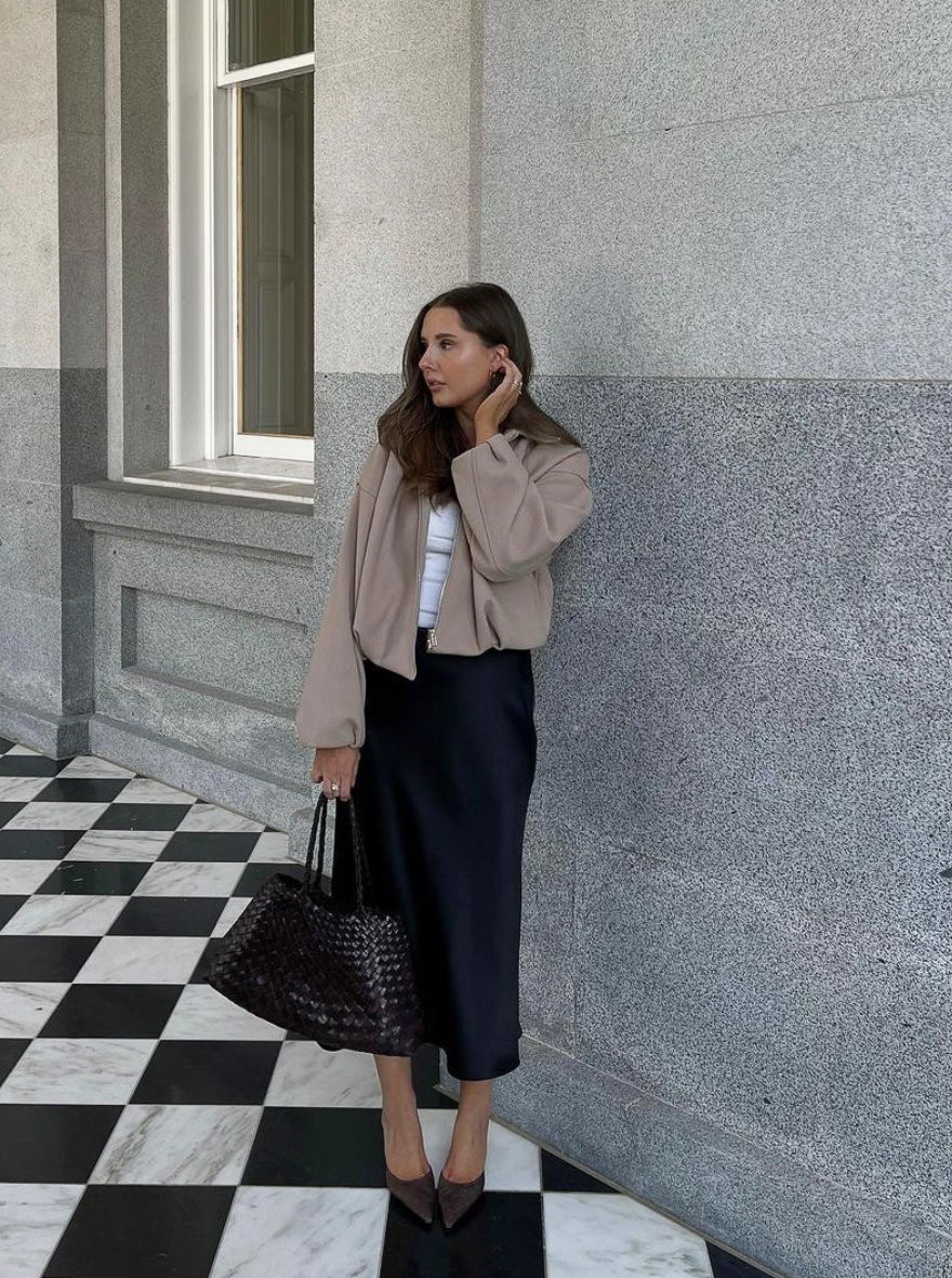 Woman wearing a black midi skirt with a brown jacket and brown heels.