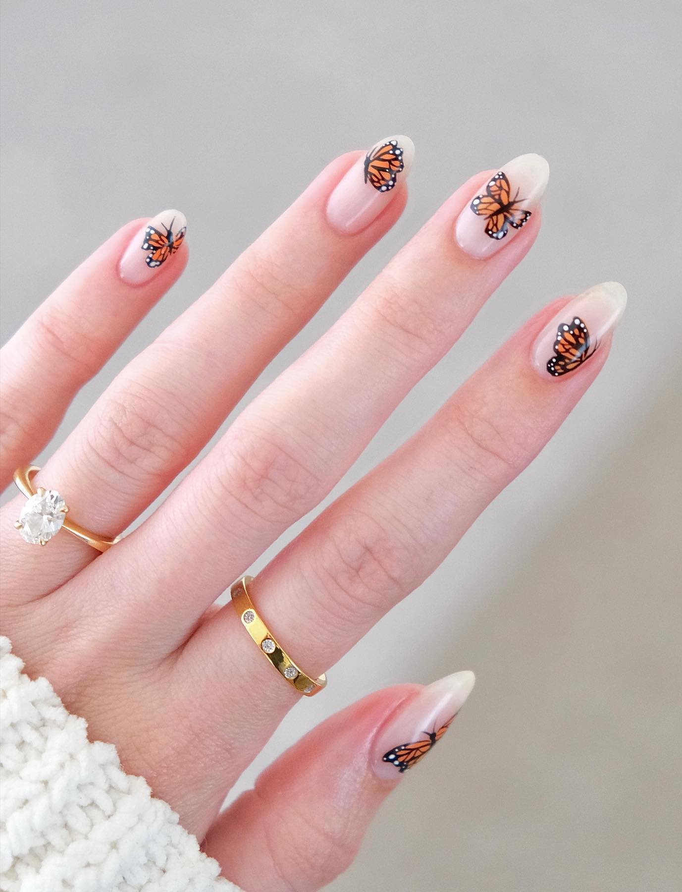 A hand with milky white almond nails with orange butterflies