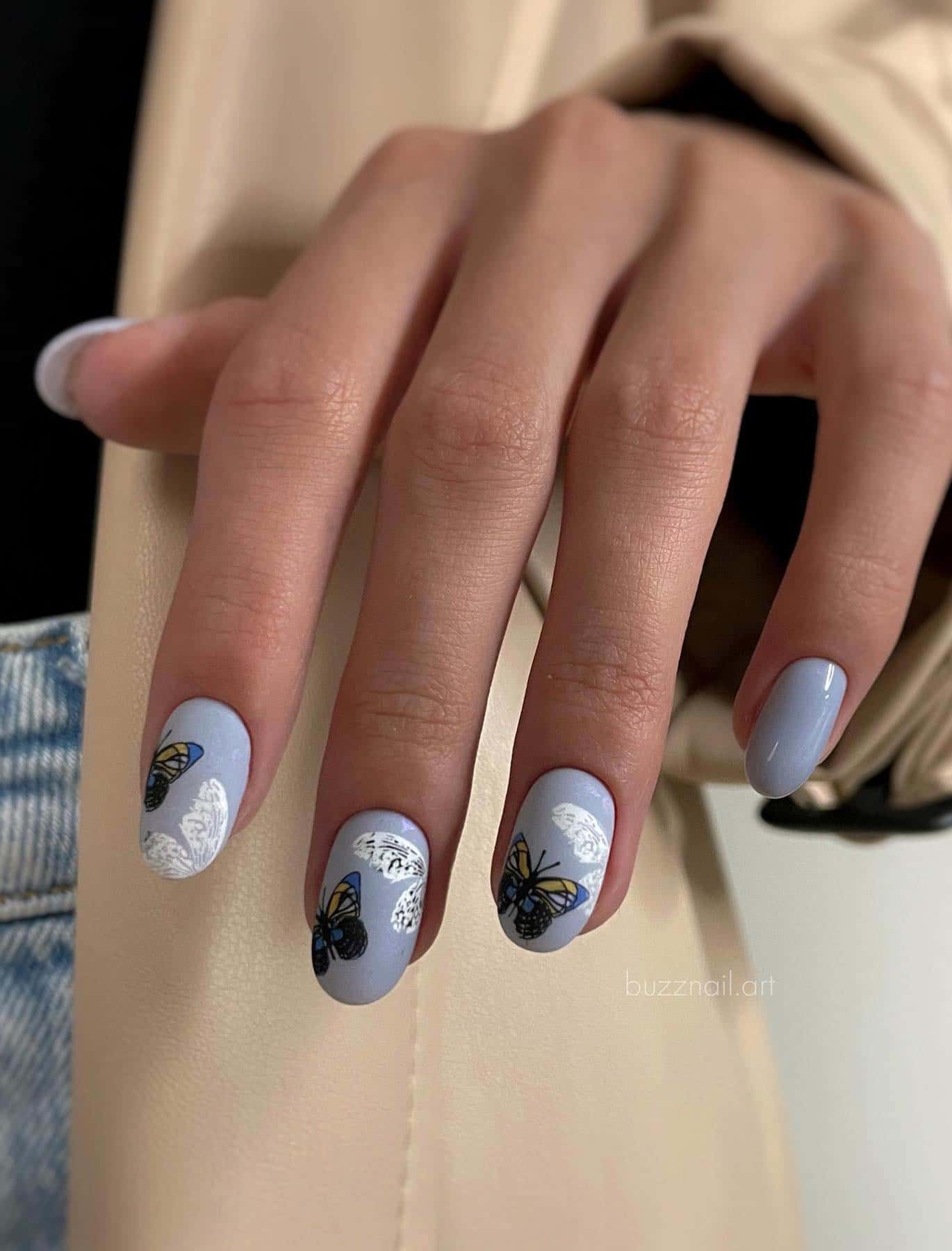 A hand with short round nails painted a light blue with white butterflies and yellow and bright blue butterflies