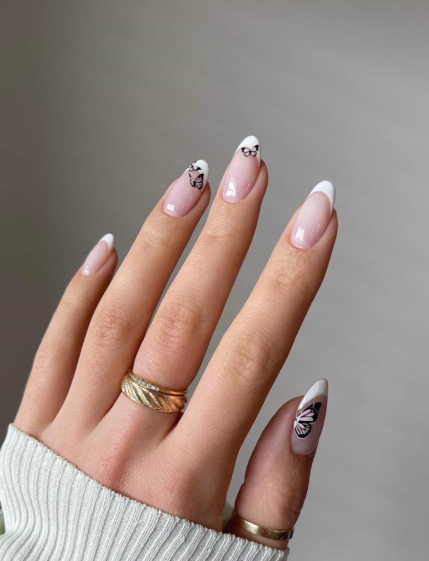A hand with short almond nails painted with a classic French manicure with pale pink butterflies
