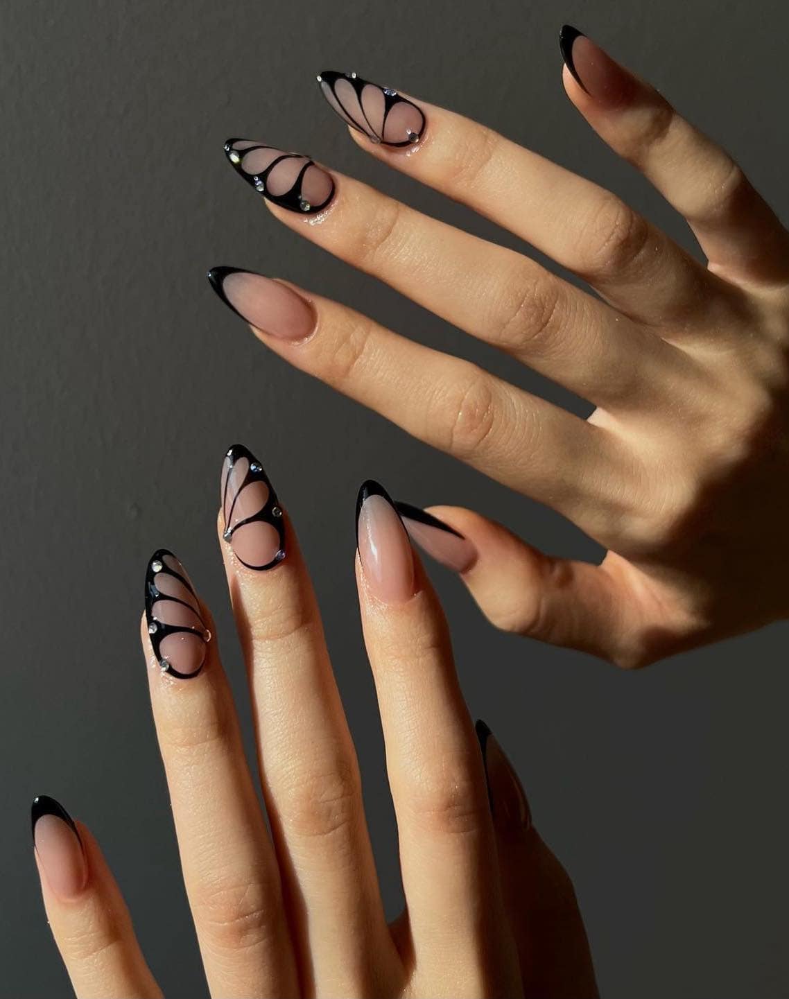 A hand with long almond nails painted a nude polish with black French tips and black butterfly wing accent nails