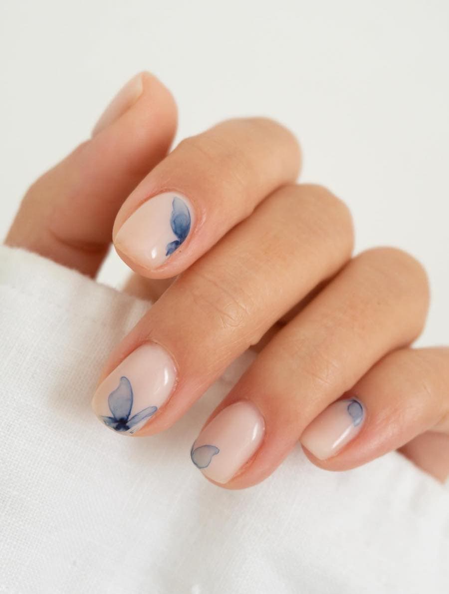 A hand with short milky white nails with translucent blue butterfly accents