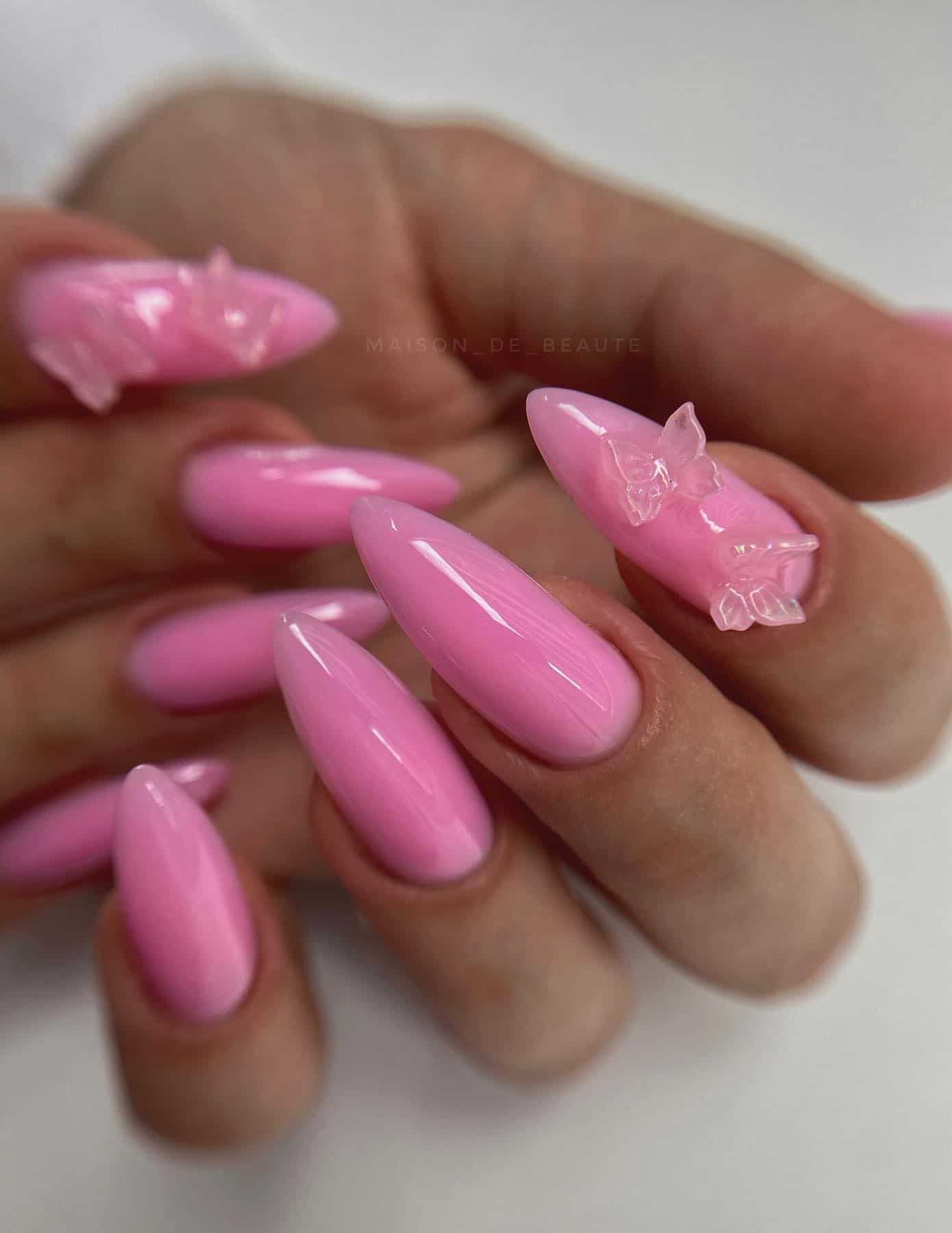 A hand with long pink almond nails with pink butterfly beads on one accent nail