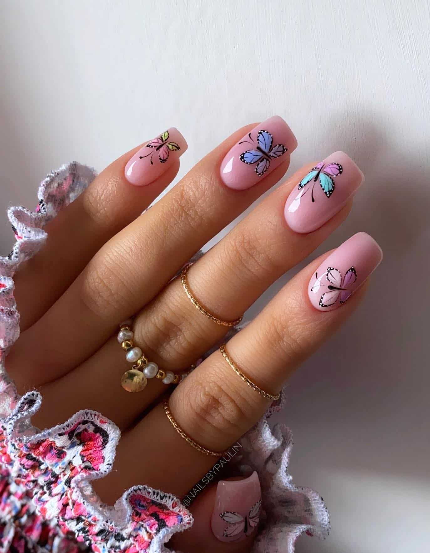 A hand with short square nails painted a light pink with colorful butterflies