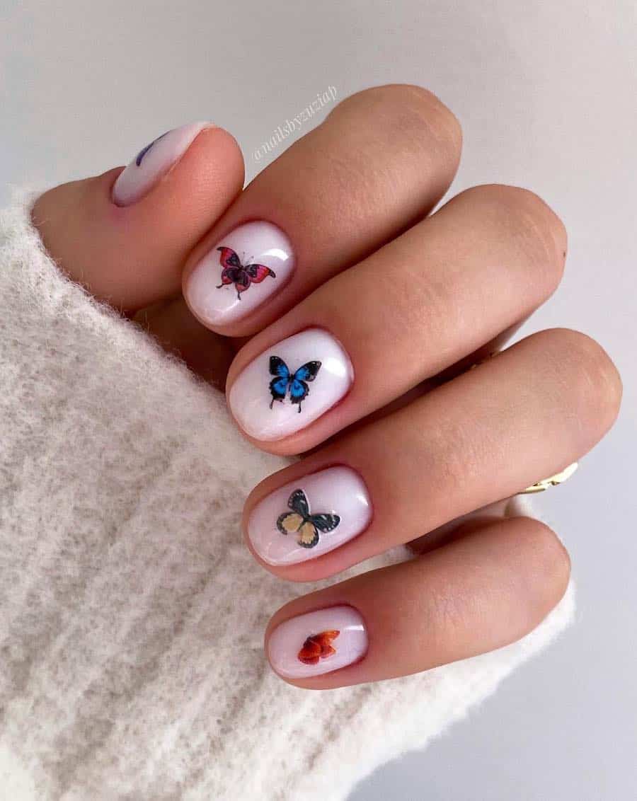 A hand with short round white nails with colorful butterflies on each nail