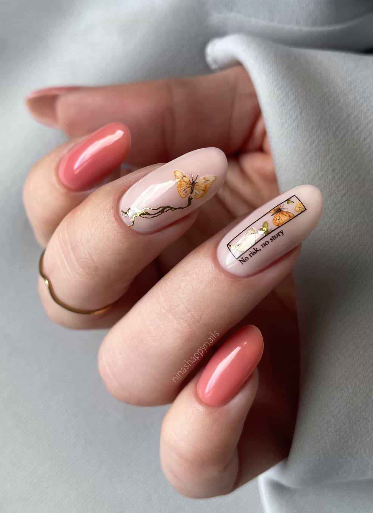 A hand with medium round nails painted a dusty pink with two pinkish white accent nails with butterfly nail art