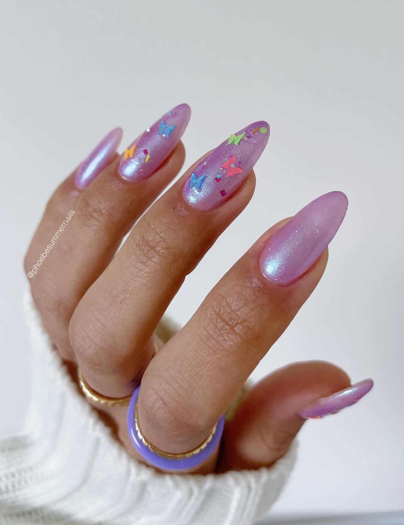A hand with long shimmering purple almond nails and two accent nails with colorful butterfly accents