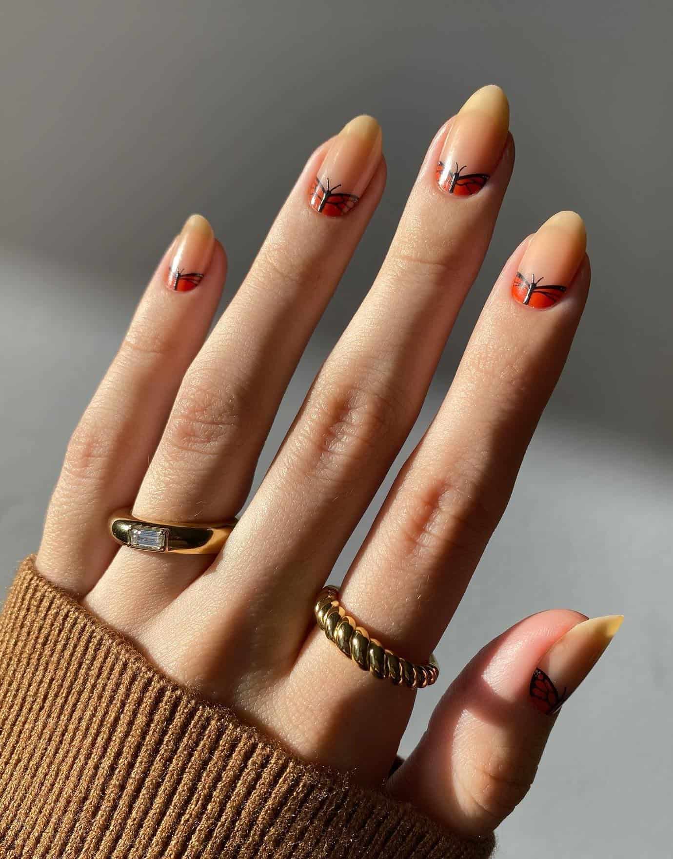 A hand with short round nude nails with orange butterfly reverse French tips
