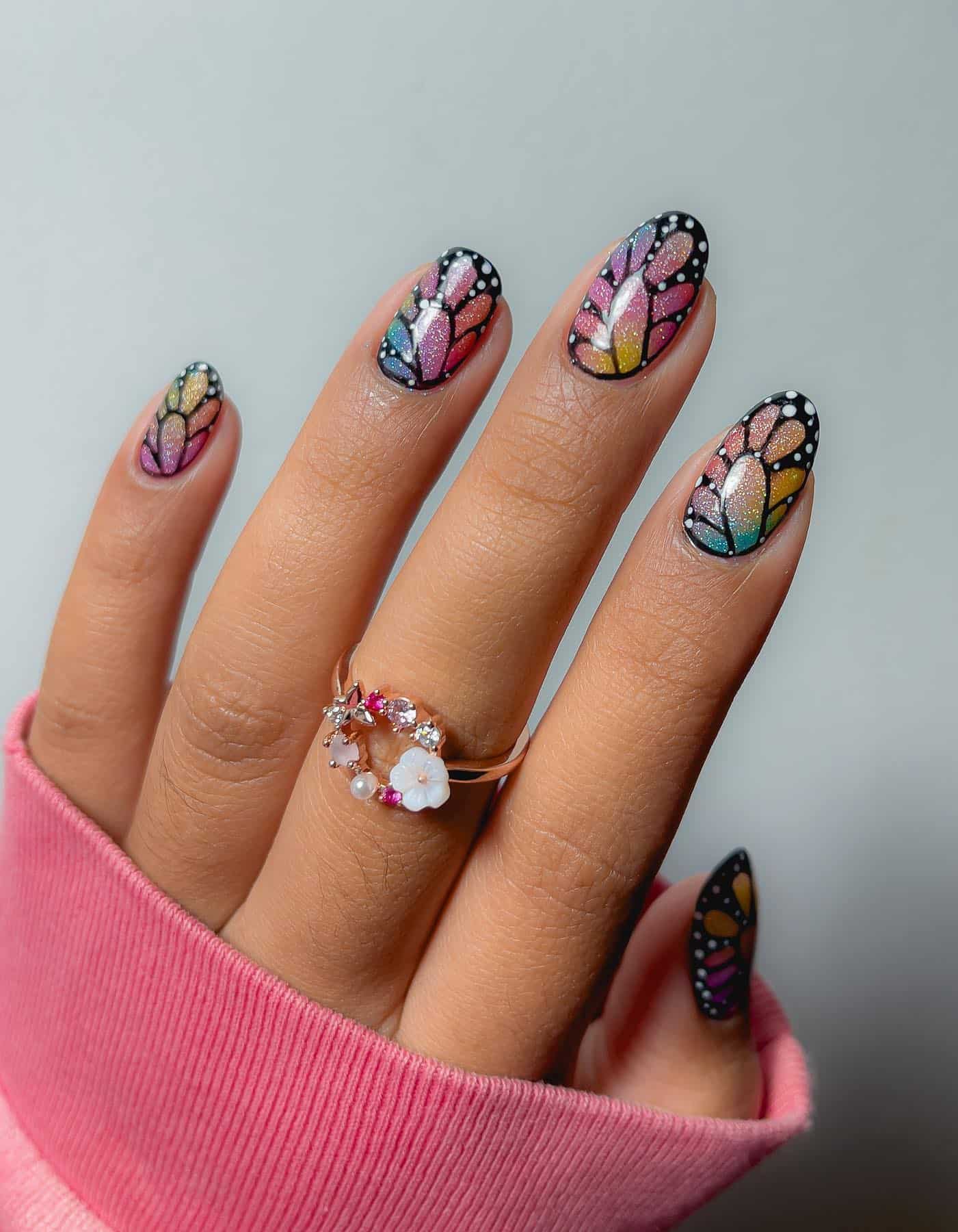 A hand with short shimmering rainbow nails with butterfly wing art over top